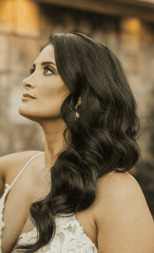 Elegant bride with wavy dark hair and sparkling earrings gazing upward in outdoor wedding portrait at The Wright House in Mesa Arizona. Taken by an Arizona Photographer.