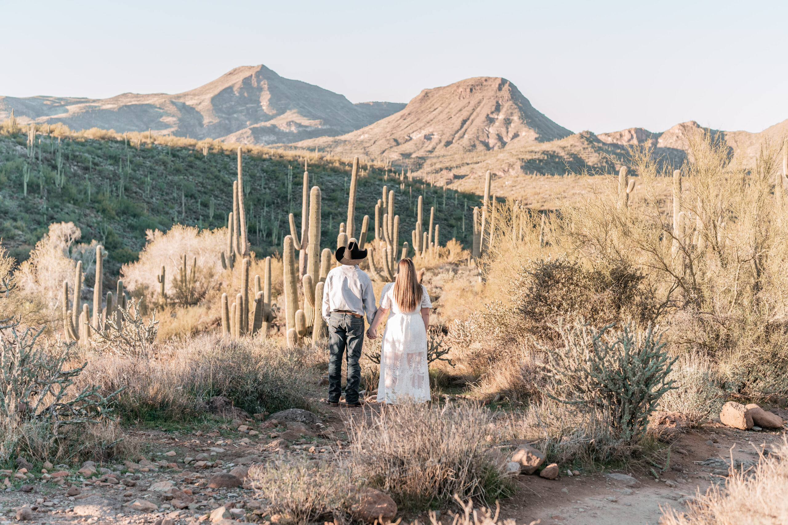 a husband and wife looking off into the distance toward big mountains as the sun is setting in the desert